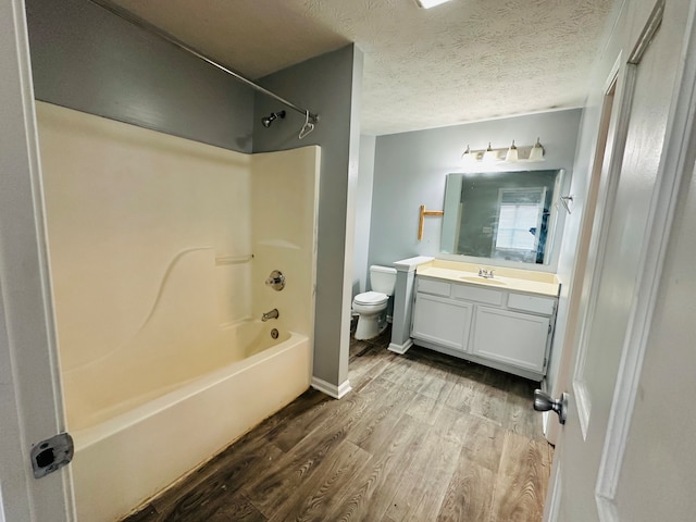 full bathroom with a textured ceiling, shower / tub combination, wood-type flooring, vanity with extensive cabinet space, and toilet