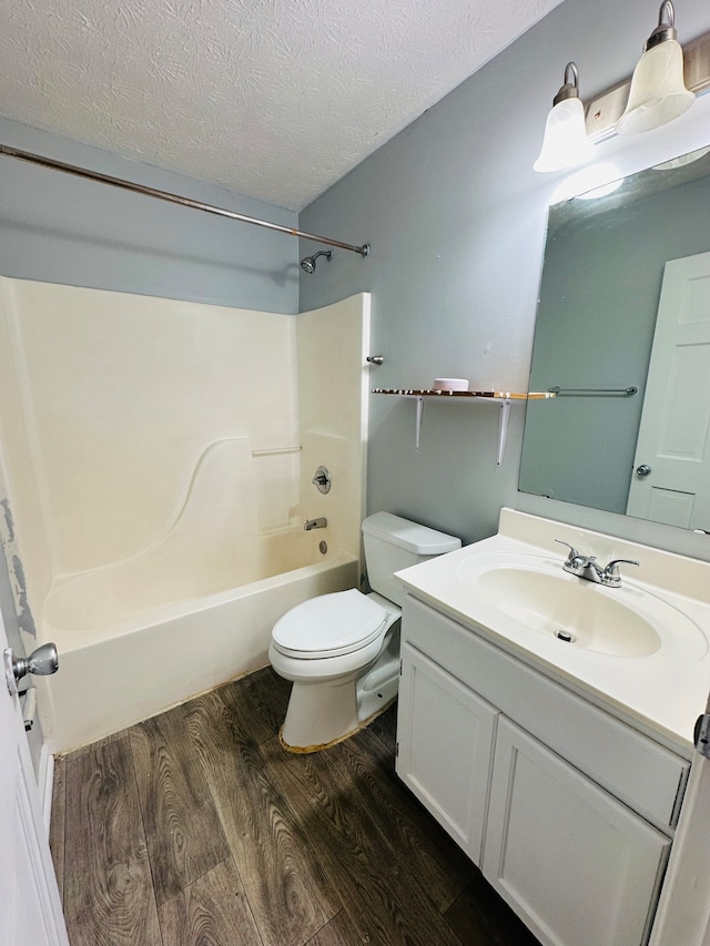 full bathroom featuring toilet,  shower combination, wood-type flooring, vanity, and a textured ceiling