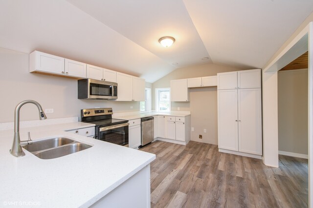 kitchen featuring vaulted ceiling, light wood-type flooring, sink, white cabinets, and appliances with stainless steel finishes