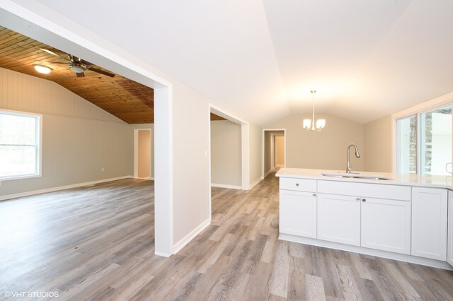 kitchen with vaulted ceiling, light hardwood / wood-style flooring, ceiling fan with notable chandelier, white cabinets, and sink