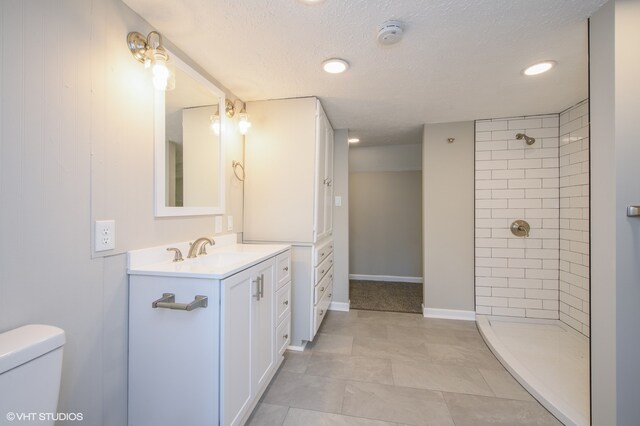 bathroom featuring a tile shower, vanity with extensive cabinet space, tile flooring, and toilet