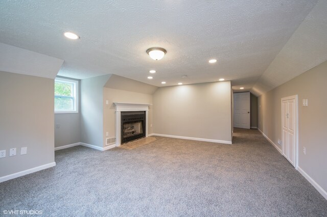 unfurnished living room featuring vaulted ceiling, a textured ceiling, and carpet floors