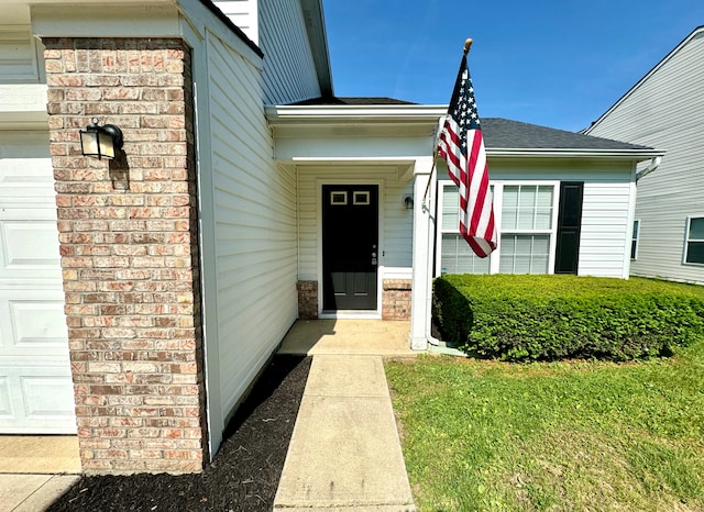 doorway to property with brick siding, an attached garage, and a shingled roof