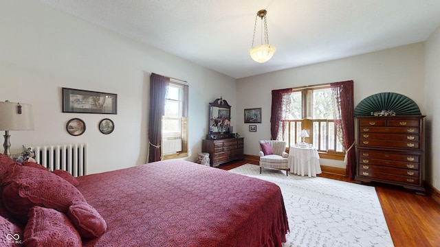 bedroom with multiple windows, wood-type flooring, and radiator heating unit