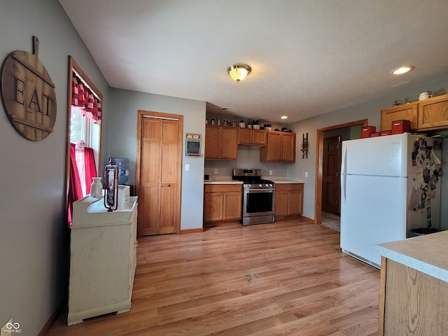 kitchen with stainless steel gas range, white fridge, and light wood-type flooring