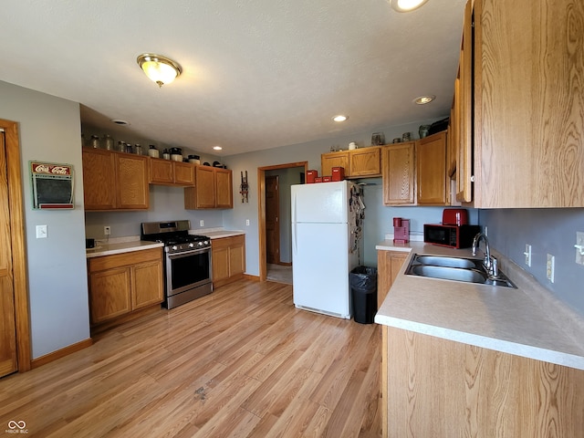 kitchen with sink, light hardwood / wood-style flooring, white refrigerator, and gas range