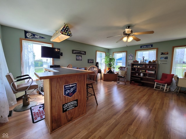 interior space with plenty of natural light, ceiling fan, a breakfast bar, and hardwood / wood-style flooring