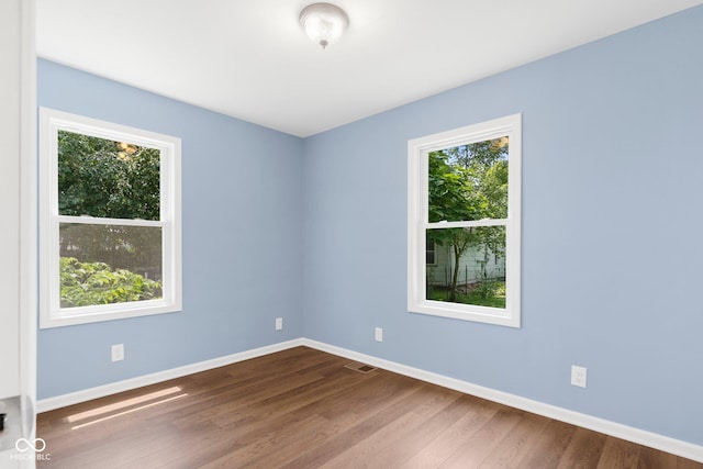 unfurnished room with visible vents, a healthy amount of sunlight, and dark wood finished floors