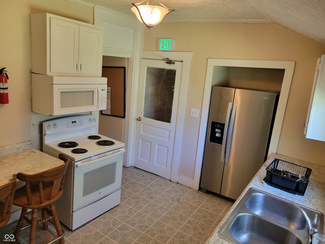 kitchen featuring white appliances, vaulted ceiling, a textured ceiling, light tile floors, and white cabinets