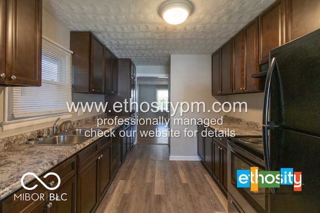 kitchen with extractor fan, hardwood / wood-style floors, light stone countertops, black refrigerator, and sink