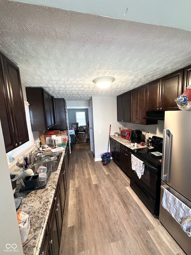 kitchen with a textured ceiling, black range with electric stovetop, stainless steel fridge, and light wood-type flooring