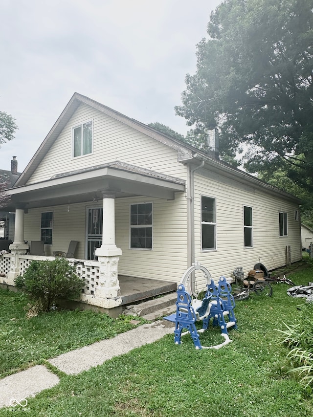 back of property with covered porch and a lawn