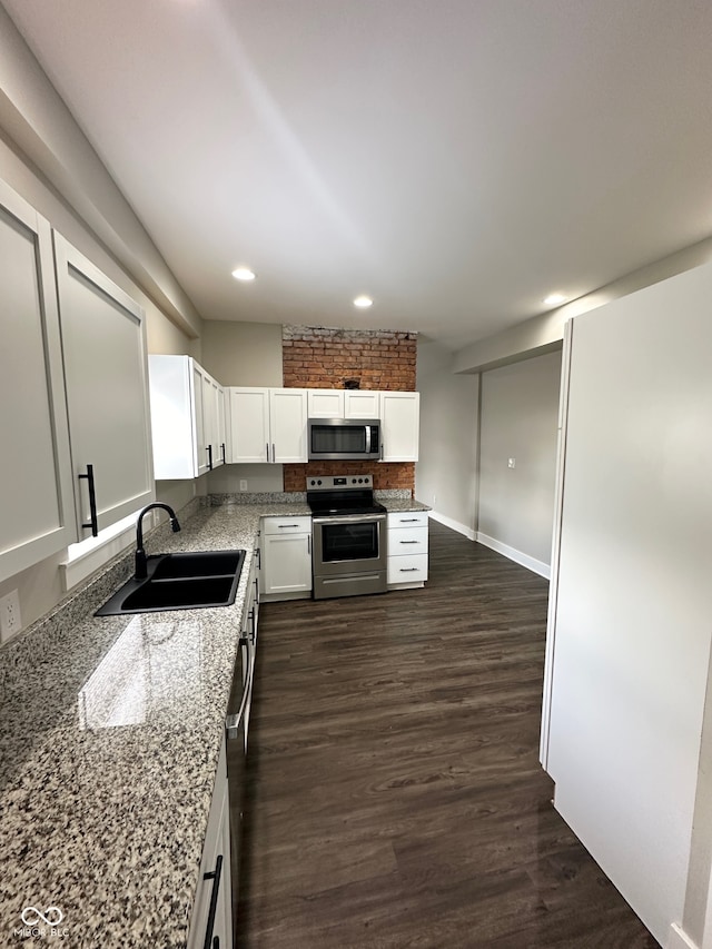 kitchen featuring dark hardwood / wood-style flooring, brick wall, sink, white cabinets, and appliances with stainless steel finishes