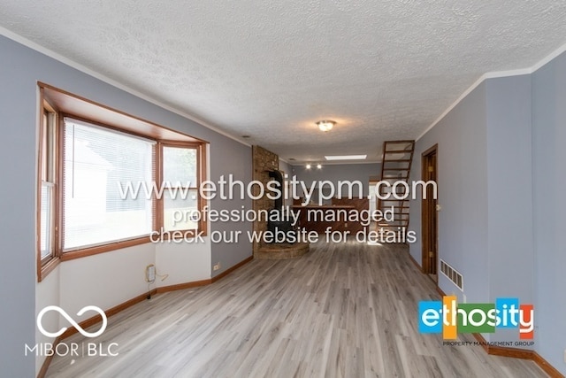 spare room featuring crown molding, wood finished floors, visible vents, and a textured ceiling