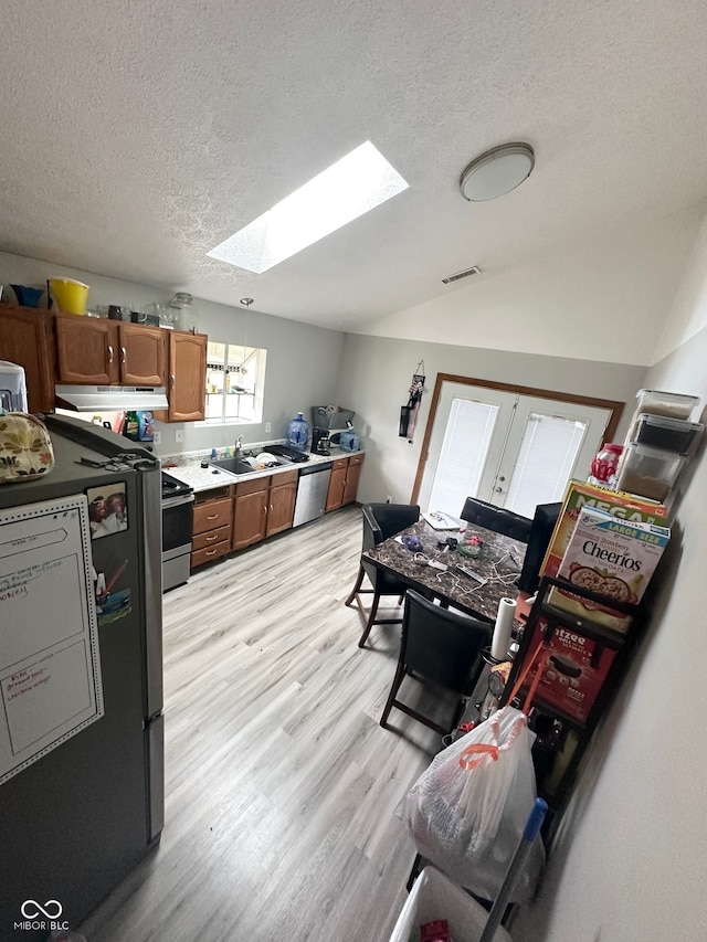 kitchen with appliances with stainless steel finishes, a textured ceiling, light wood-type flooring, and a skylight