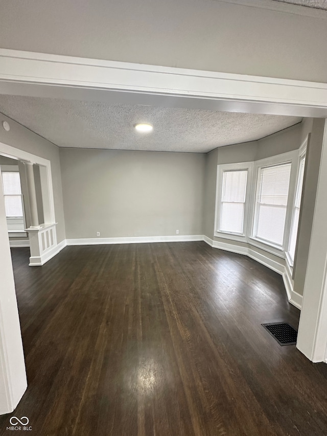 spare room with a wealth of natural light, a textured ceiling, and dark hardwood / wood-style floors