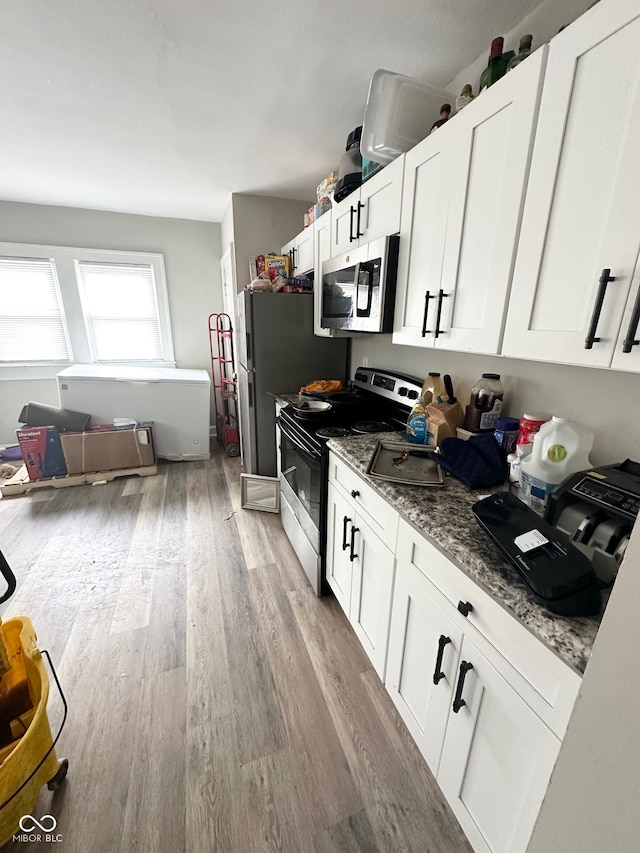 kitchen with stainless steel appliances, white cabinetry, stone counters, and light wood-type flooring