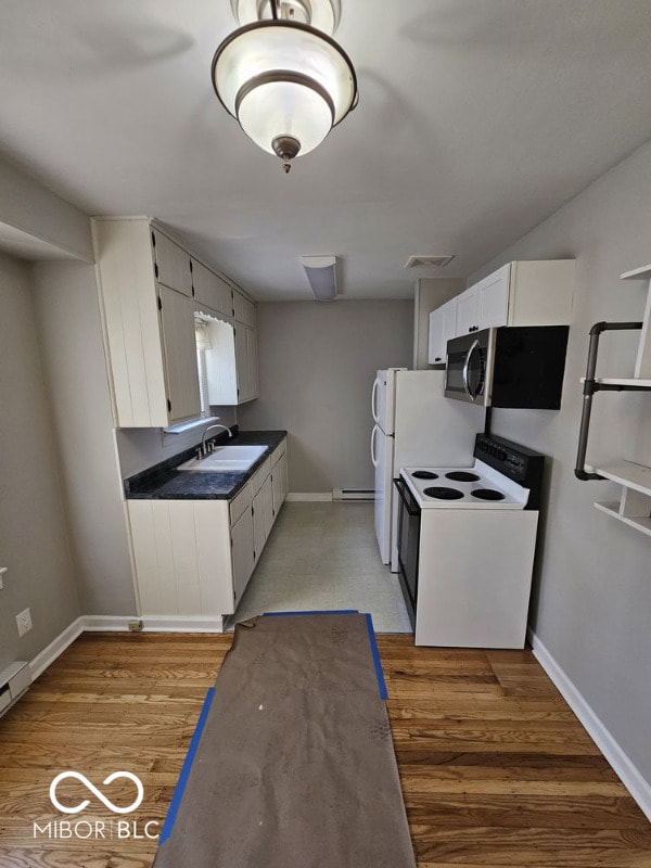 kitchen with light wood-style flooring, stainless steel microwave, dark countertops, a sink, and white range with electric cooktop
