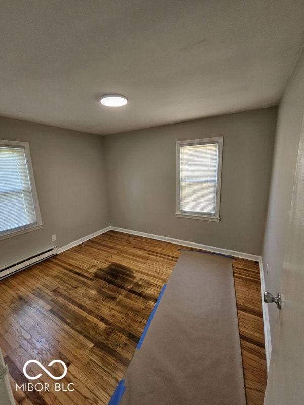 unfurnished room with baseboards, baseboard heating, and wood finished floors