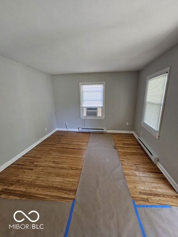 unfurnished room featuring a healthy amount of sunlight, hardwood / wood-style floors, and a baseboard radiator