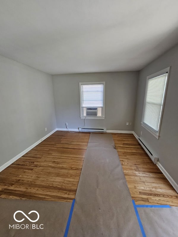 unfurnished room with baseboard heating, wood finished floors, and a healthy amount of sunlight