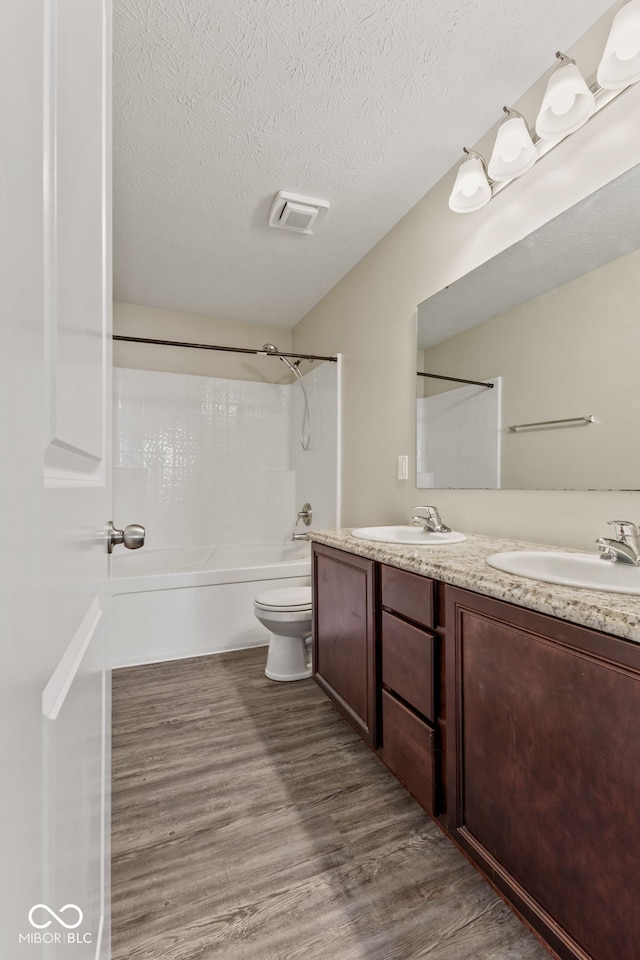 full bathroom with vanity, a textured ceiling, shower / washtub combination, hardwood / wood-style floors, and toilet