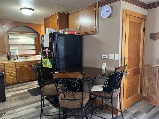 kitchen with crown molding, black fridge, sink, and light wood-type flooring