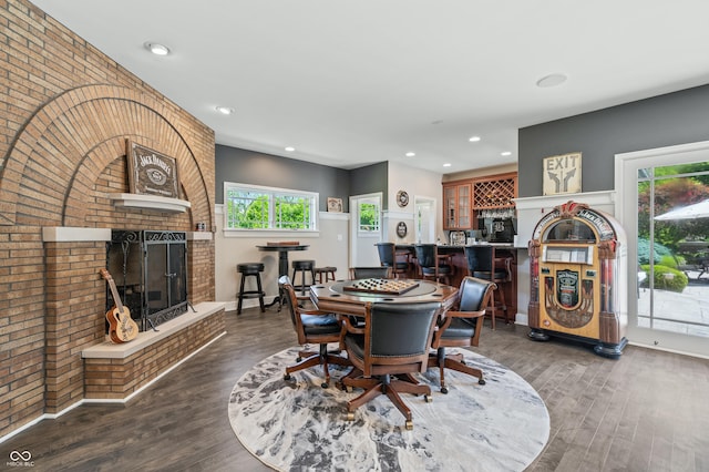 dining area featuring dark hardwood / wood-style flooring, indoor bar, brick wall, and a brick fireplace