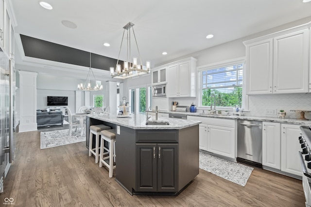 kitchen with white cabinetry, stainless steel appliances, dark hardwood / wood-style flooring, decorative light fixtures, and a center island with sink