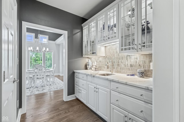 bar featuring backsplash, light stone counters, dark wood-type flooring, sink, and white cabinetry