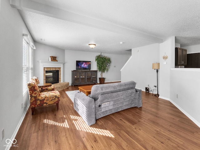 living room featuring hardwood / wood-style flooring, a textured ceiling, beamed ceiling, and a brick fireplace