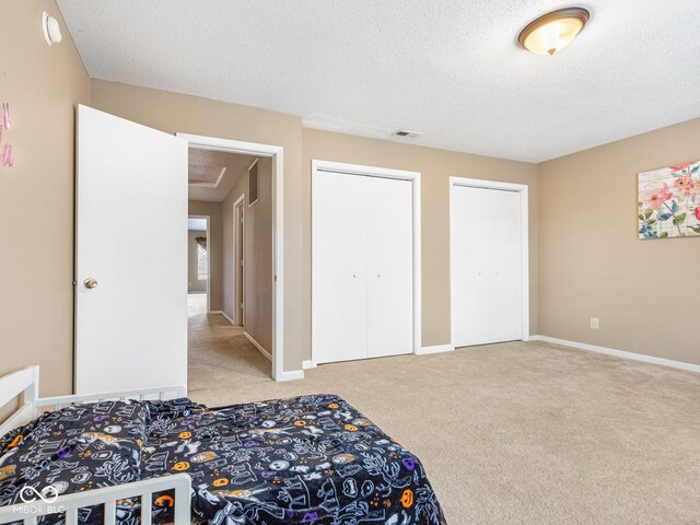 bedroom with a textured ceiling, light carpet, and two closets