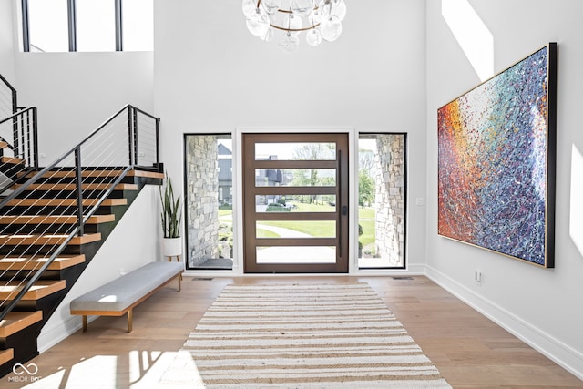 entryway with a notable chandelier, light hardwood / wood-style floors, and a towering ceiling