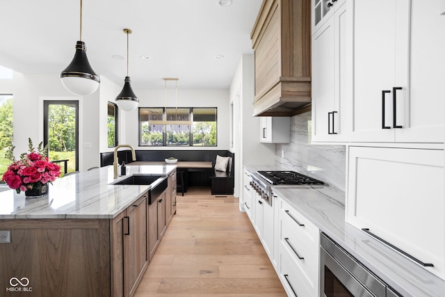 kitchen featuring light stone countertops, an island with sink, white cabinetry, and sink