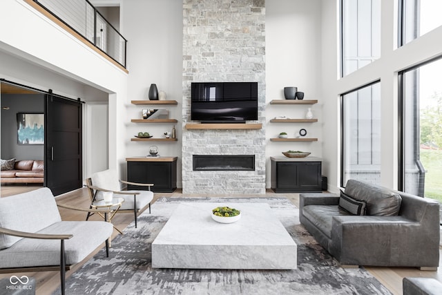 living room featuring a barn door, wood-type flooring, a fireplace, and a high ceiling