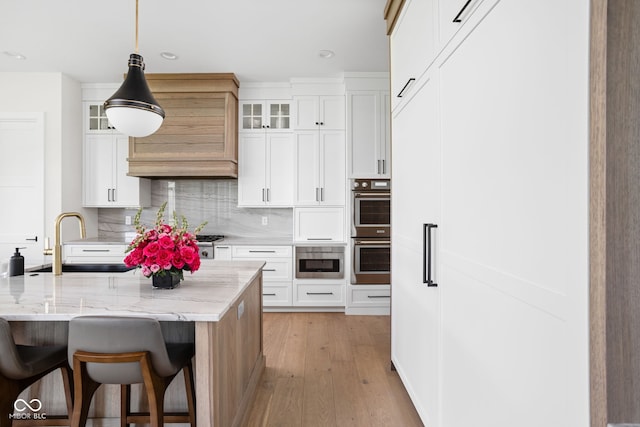 kitchen featuring white cabinetry, sink, light stone countertops, an island with sink, and pendant lighting