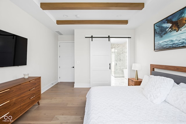 bedroom with a barn door, ensuite bathroom, and light wood-type flooring