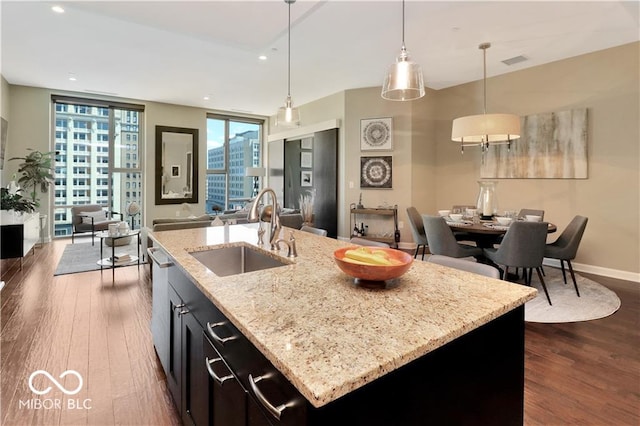 kitchen with a center island with sink, pendant lighting, dark wood-type flooring, sink, and floor to ceiling windows