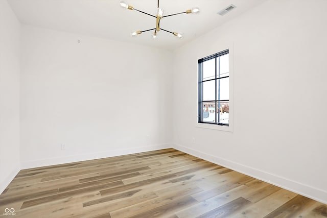 spare room featuring light wood-type flooring and an inviting chandelier