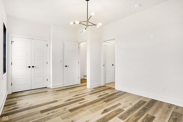 unfurnished bedroom with light hardwood / wood-style flooring, a closet, and a notable chandelier