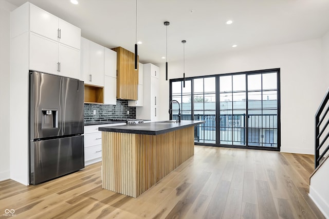 kitchen featuring stainless steel fridge with ice dispenser, an island with sink, pendant lighting, white cabinets, and light wood-type flooring