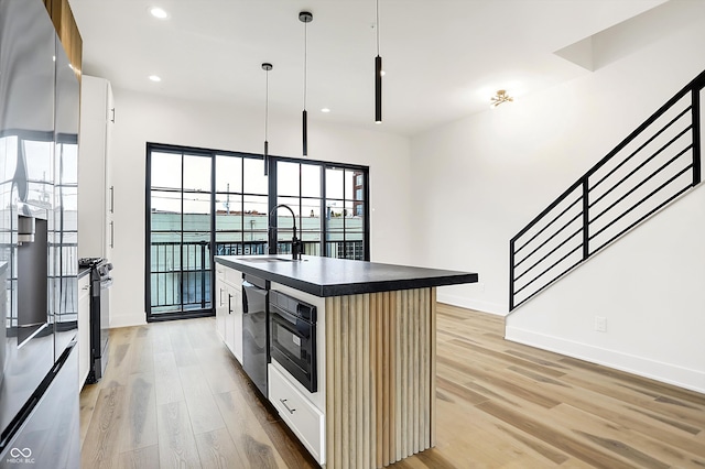 kitchen featuring light wood-type flooring, sink, pendant lighting, white cabinets, and an island with sink