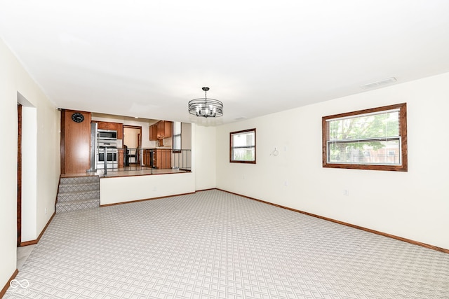 unfurnished living room featuring a notable chandelier, light colored carpet, and a wealth of natural light