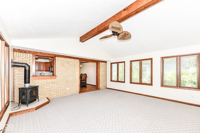 unfurnished living room featuring ceiling fan, lofted ceiling with beams, a wood stove, and carpet