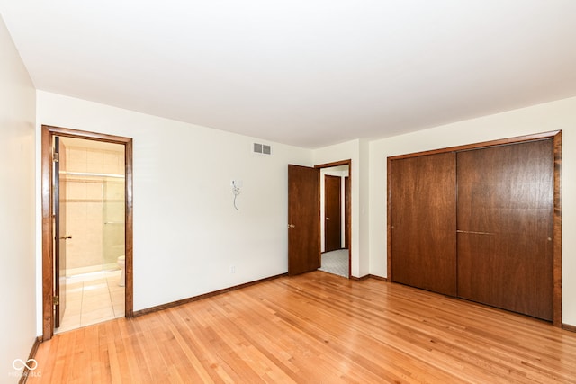 unfurnished bedroom with ensuite bathroom, a closet, and light wood-type flooring