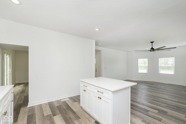 kitchen with light wood-type flooring, ceiling fan, a kitchen island, and white cabinets