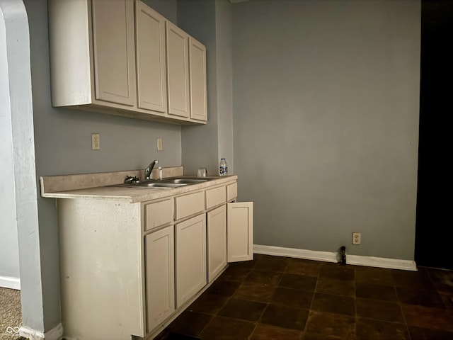 kitchen featuring light countertops, a sink, white cabinets, and baseboards