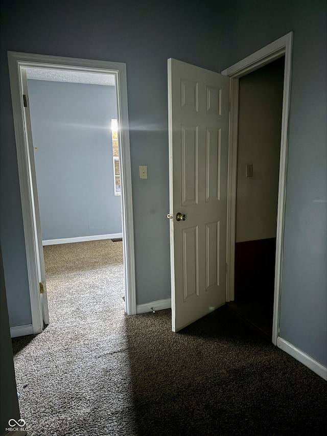 hall with dark colored carpet and baseboards