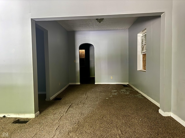 spare room featuring dark colored carpet, arched walkways, baseboards, and a textured ceiling