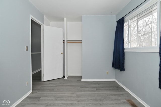 unfurnished bedroom with a closet, visible vents, baseboards, and wood finished floors